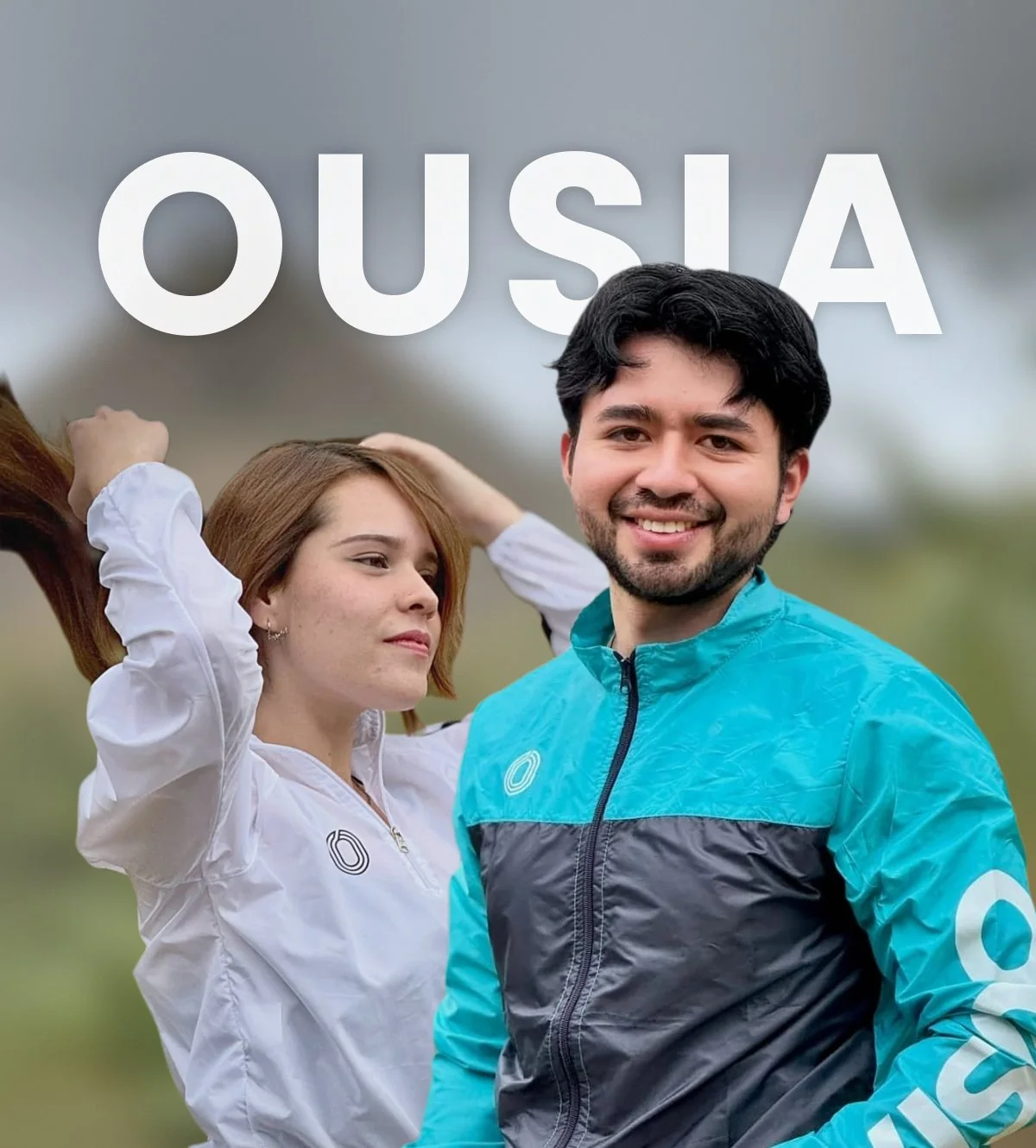 Un hombre sonriendo al frente con la chompa bicolor turquesa y negra, y una mujer con la chompa blanca de medio cierre detrás, bajo la palabra OUSIA