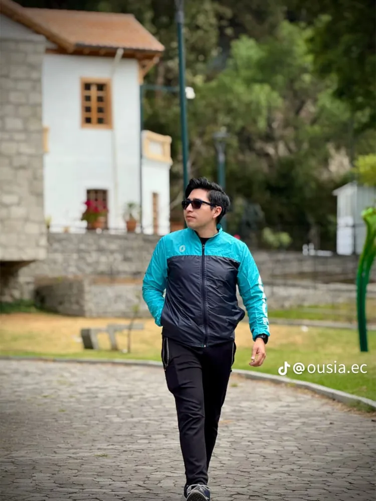 Hombre caminando con chompa turquesa y negra en el parque